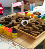 A child's work table- with wooden large alphabets and small paint containers.