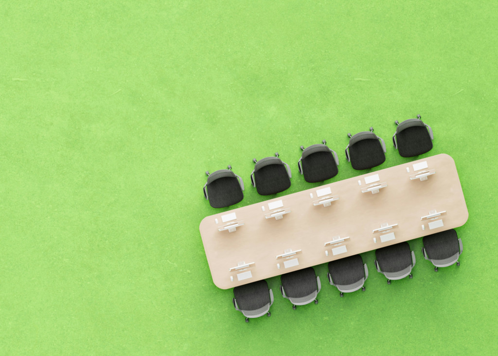 Overhead view of a long meeting table with chairs on a bright green floor.
