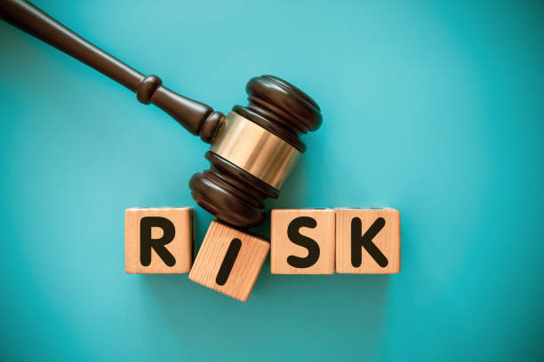 The word RISK, spelt out from left to right in wooden building blocks with one letter on each building block. The building blocks are being hit with a legal hammer, placed in front of a plain blue background