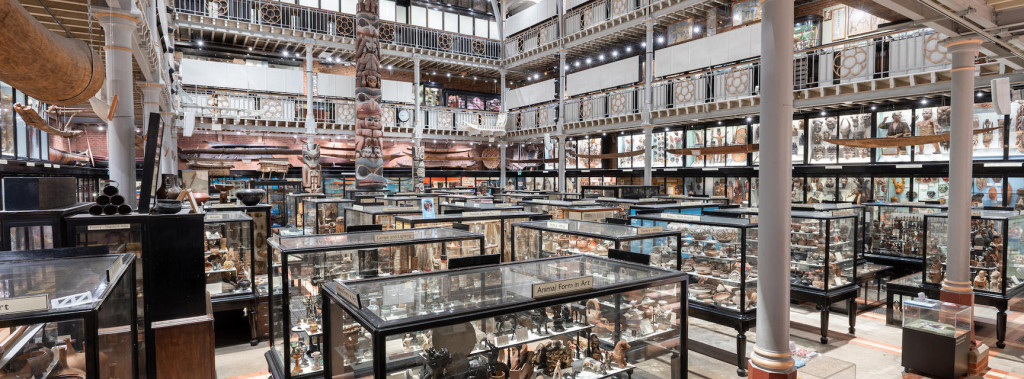 Interior of the Pitt Rivers Museum, Oxford, showing rows of glass display cases filled with historical and cultural artefacts, surrounded by multi-level galleries.