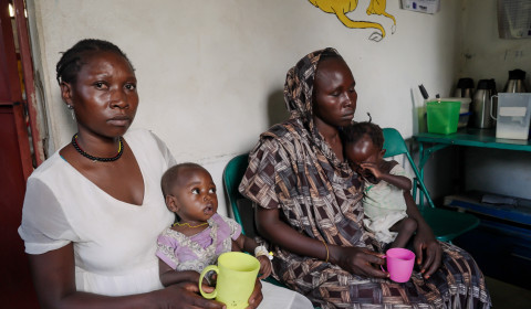 Two mothers sit in their kitchen with very young children on their laps