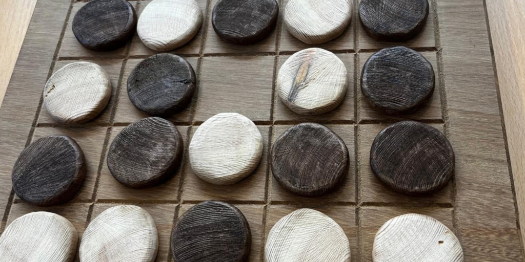 Photograph of a wooden draughts board with black and white circular counters on it