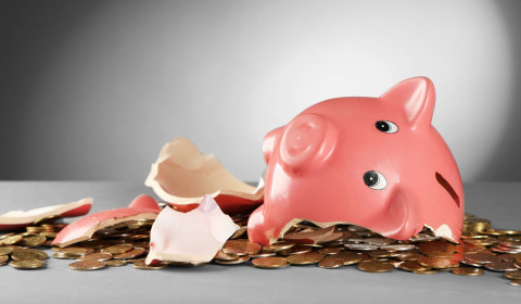 Photograph of a broken piggy bank with coins spilled from it onto the table